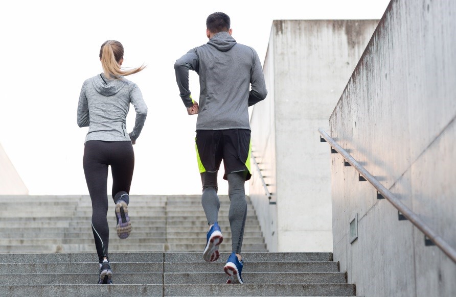 En kvinde og en mand iført træningstøj løber op ad en trappe.