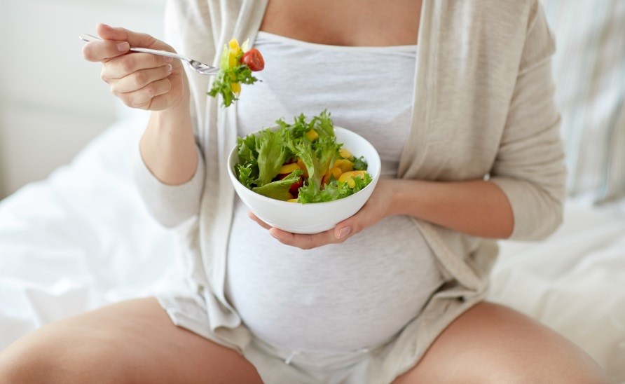Gravid kvinde, der spiser salat.